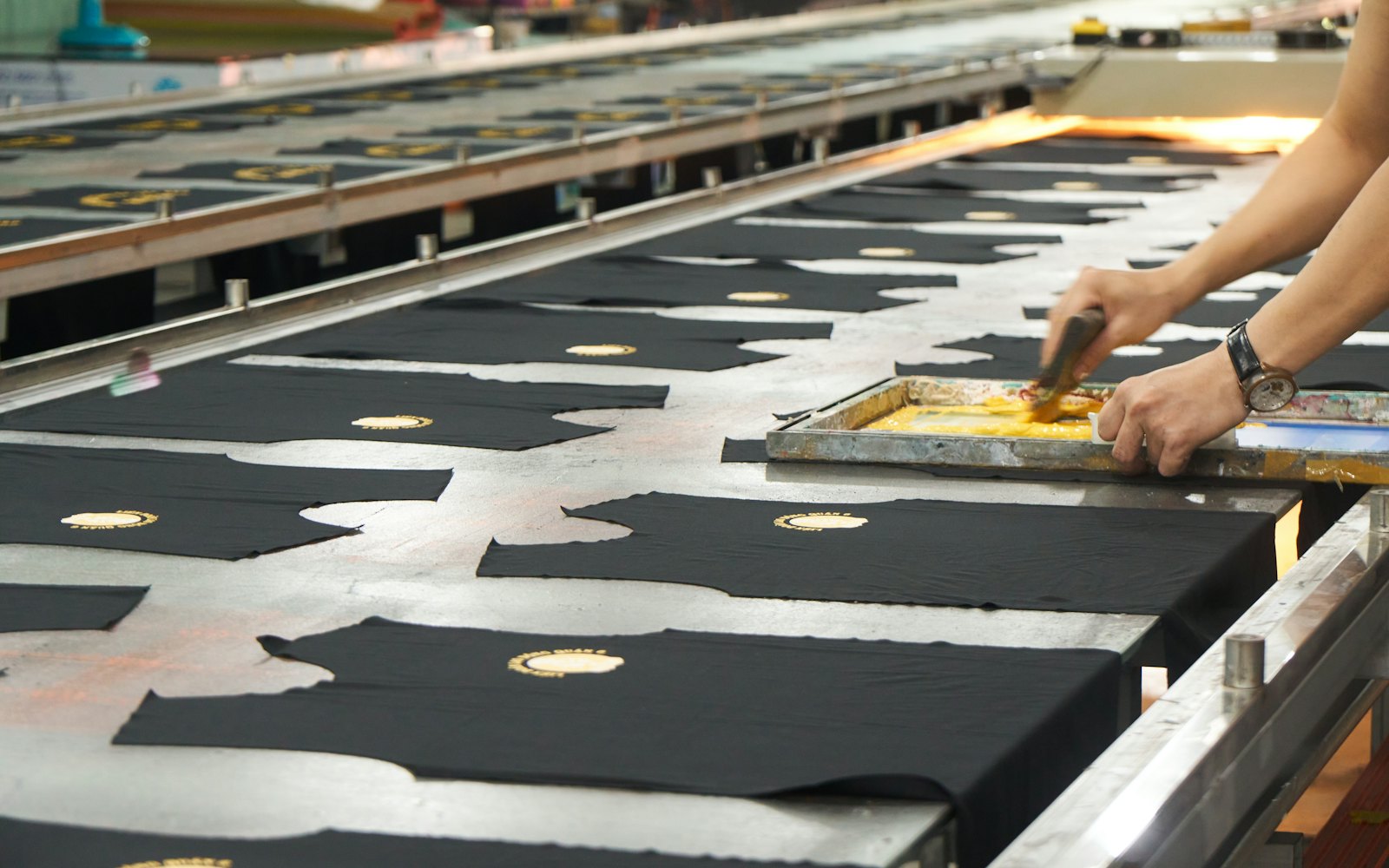Black t-shirts being screen printed on a long production line