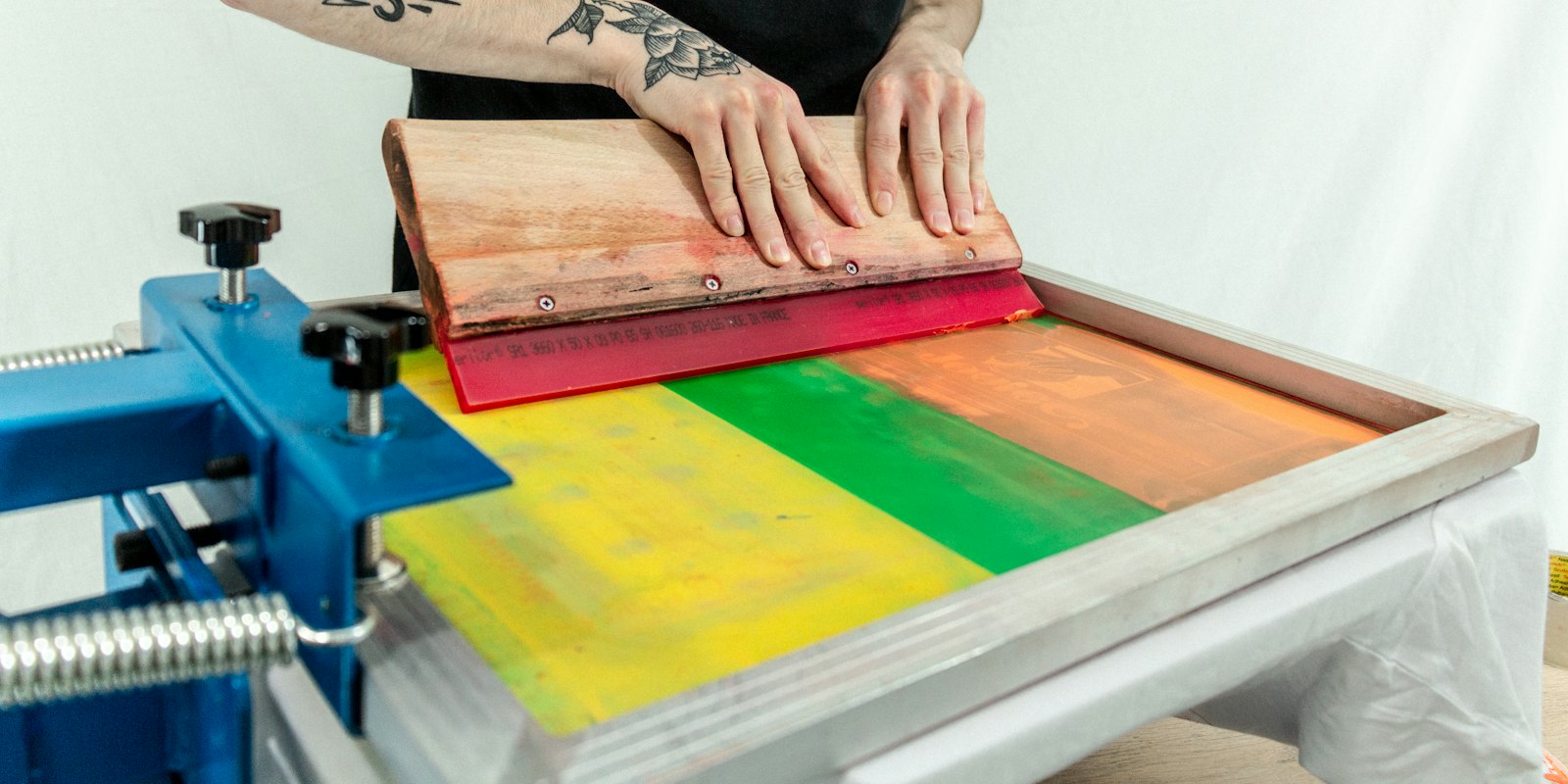 Hands pulling a squeegee across a screen printing press