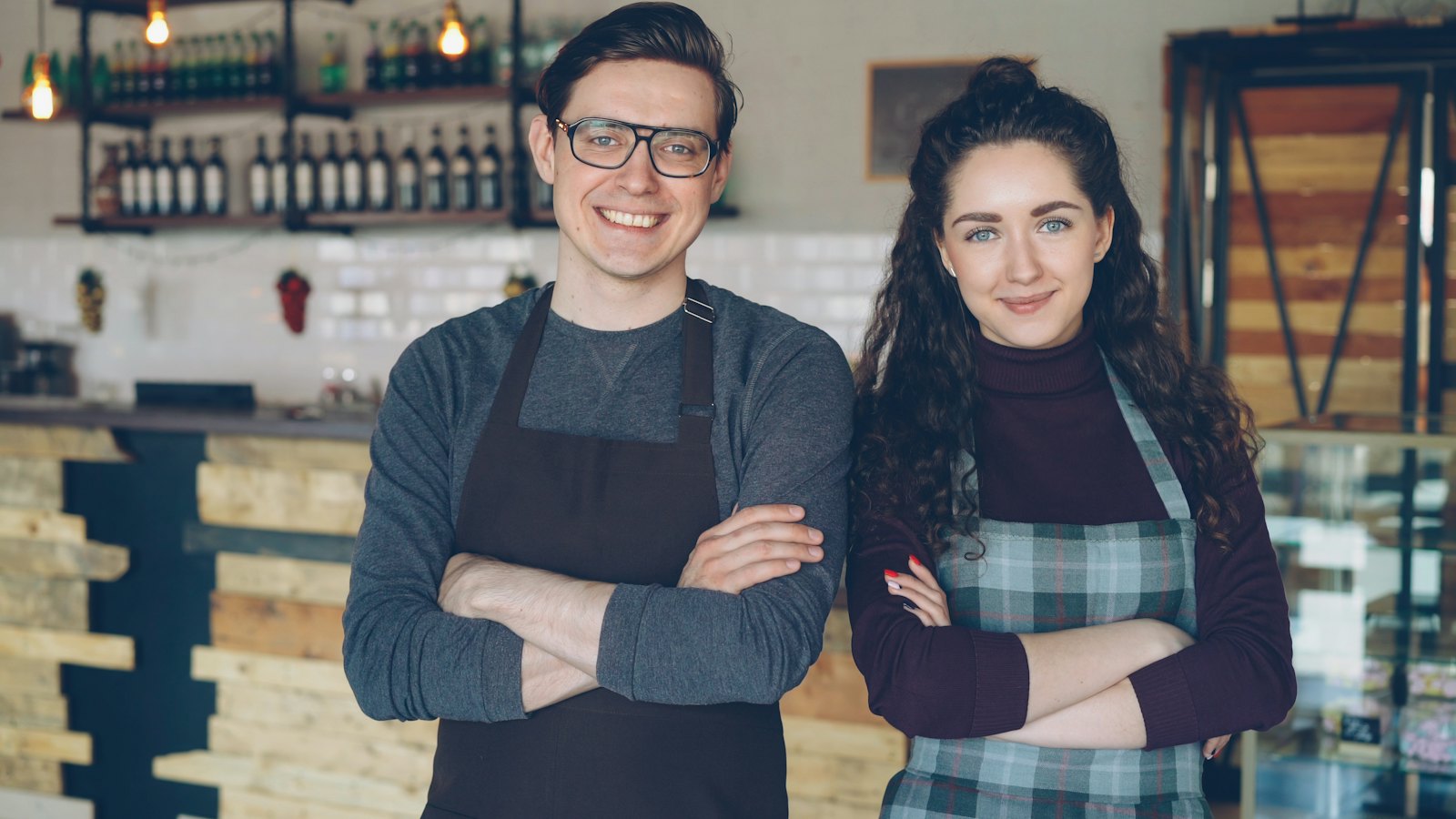 Two cafe owners in aprons standing behind their counter